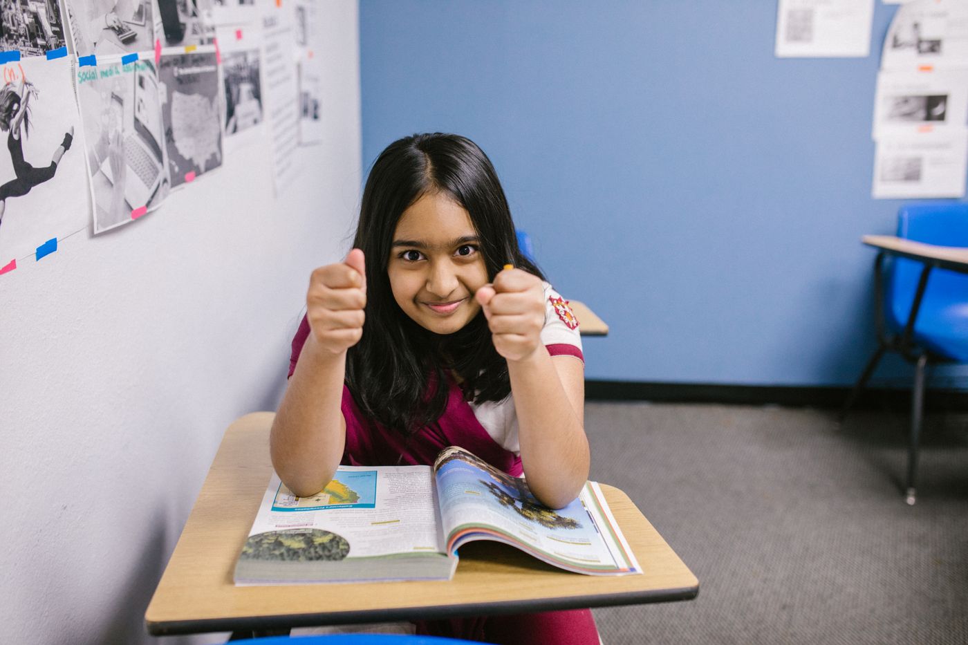 A smiling schoolgirl giving a thumbs up at her desk
