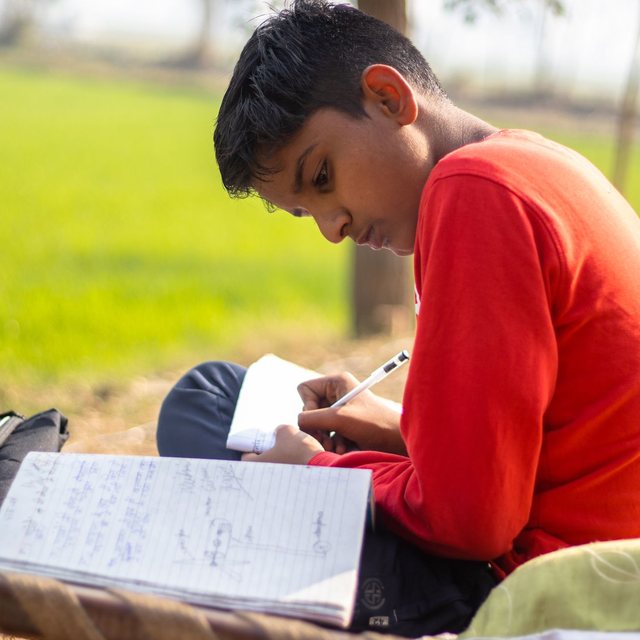 A boy concentrating on his homework, writing in his notebook